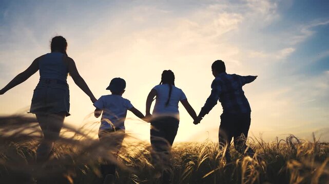 Silhouette of family walking through field. Family walking in a field at sunset. Silhouette of a young woman bonding with her friends outside the forest. Outline of a family strolling lifestyle.