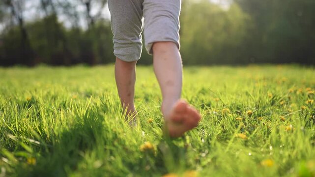 Person walking through field. Barefoot child walking in the grass at park. A kid is taking a walk in a park. An individual strolling lifestyle across a pasture.