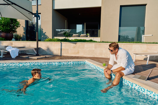 Father and Son Enjoying Morning at Private Pool Beside Modern Luxury Home Patio
