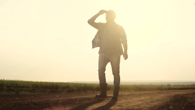 Man walking down dirt road. Silhouette of farmer walking in a field. Farmer working on a lifestyle field in evening. A individual strolling along a unpaved path.