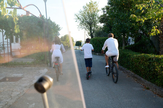 Family Biking and Scootering Together on a Quiet Residential Street During Summer Vacation