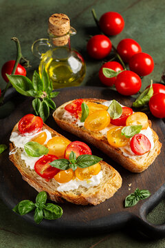 Toasted Italian bread, or bruschetta, with creamy stracciatella cheese and red and yellow cherry tomatoes. Mediterranean appetizer, homemade. Vertical image.