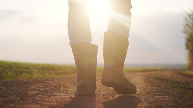 Person walking down dirt road. Man working on his boots in a field. Close up of a farmer walking his legs up a lifestyle road. An individual strolling along a gravel path.