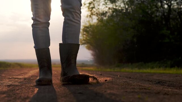 Person walking down dirt road. Man working on his boots in a field. Lifestyle close up of a farmer walking his legs up a road. An individual strolling along a gravel path.