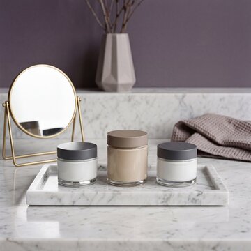 Set of blank cosmetic cream jars on white marble tray with golden mirror, vase and soft towel on elegant vanity counter for skincare packaging mockup.