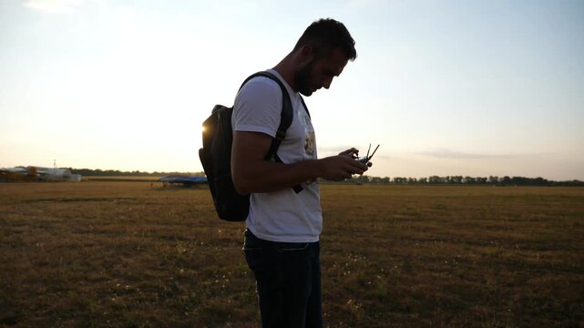 Man with backpack stands in open field, preparing to launch drone, showcasing the excitement of aerial exploration and technology in a serene outdoor environment