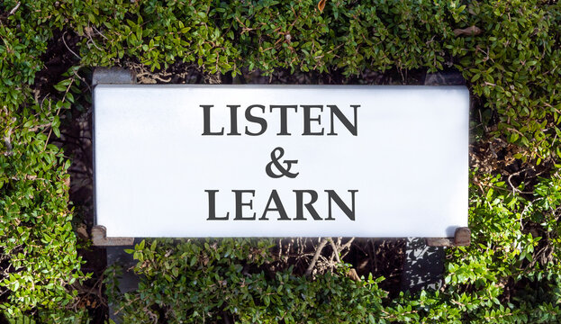 Listen and learn words symbol. Concept words Listen and learn on beautiful white sign plate. Beautiful green trees background. Business listen and learn support concept. Copy space.