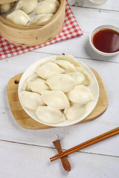 Fresh Handmade Chinese Dumplings with Bamboo Steamer and Soy Sauce on White Wooden Background
