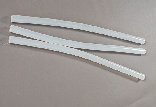 A professional, high-resolution commercial studio shot showcasing clear translucent hot melt glue sticks arranged neatly on a matte neutral grey surface