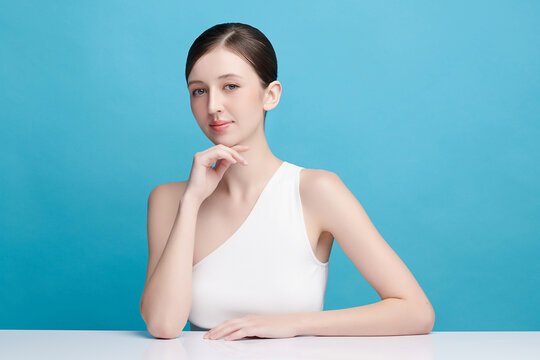 A beautiful young Asian woman with clean, fresh skin against a blue background. Skincare, facial treatment, cosmetology, beauty, and spa. An elegant portrait of an Asian woman.
