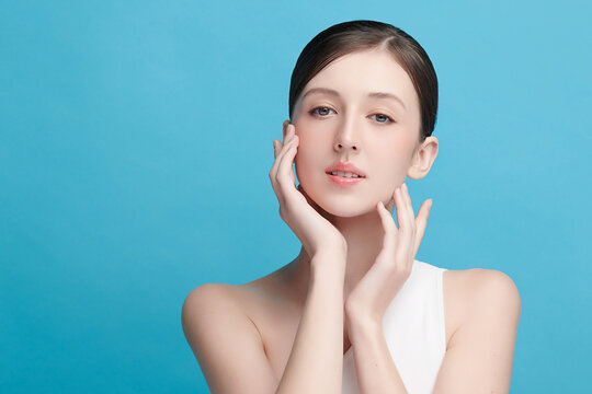 A beautiful young Asian woman with clean, fresh skin against a blue background. Skincare, facial treatment, cosmetology, beauty, and spa. An elegant portrait of an Asian woman.