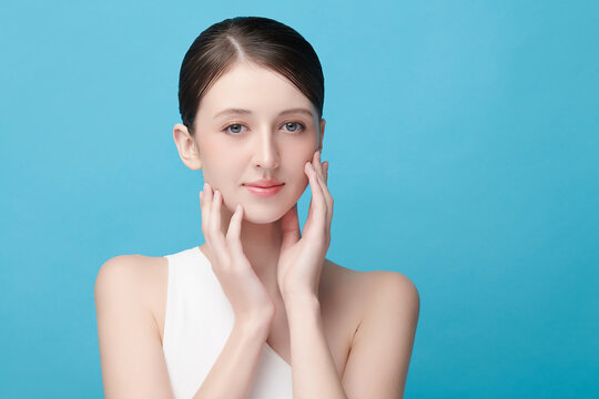 A beautiful young Asian woman with clean, fresh skin against a blue background. Skincare, facial treatment, cosmetology, beauty, and spa. An elegant portrait of an Asian woman.