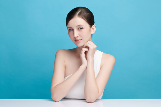 A beautiful young Asian woman with clean, fresh skin against a blue background. Skincare, facial treatment, cosmetology, beauty, and spa. An elegant portrait of an Asian woman.