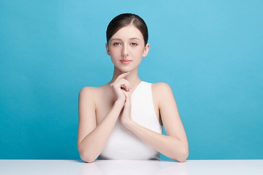 A beautiful young Asian woman with clean, fresh skin against a blue background. Skincare, facial treatment, cosmetology, beauty, and spa. An elegant portrait of an Asian woman.