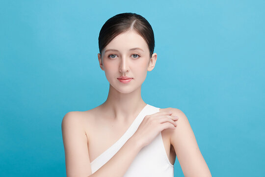 A beautiful young Asian woman with clean, fresh skin against a blue background. Skincare, facial treatment, cosmetology, beauty, and spa. An elegant portrait of an Asian woman.