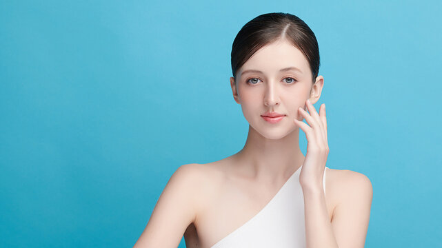 A beautiful young Asian woman with clean, fresh skin against a blue background. Skincare, facial treatment, cosmetology, beauty, and spa. An elegant portrait of an Asian woman.