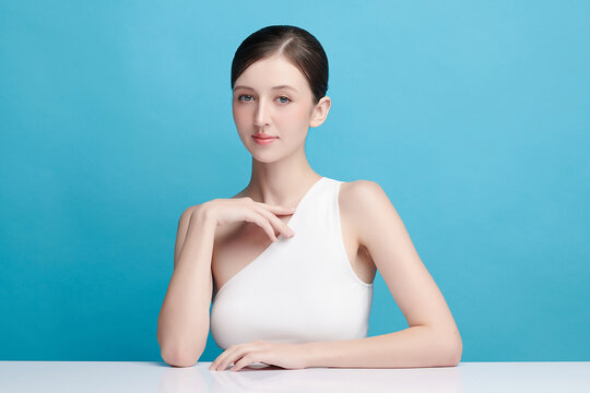 A beautiful young Asian woman with clean, fresh skin against a blue background. Skincare, facial treatment, cosmetology, beauty, and spa. An elegant portrait of an Asian woman.