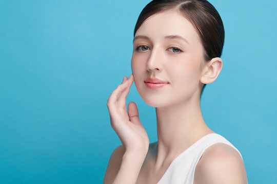 A beautiful young Asian woman with clean, fresh skin against a blue background. Skincare, facial treatment, cosmetology, beauty, and spa. An elegant portrait of an Asian woman.