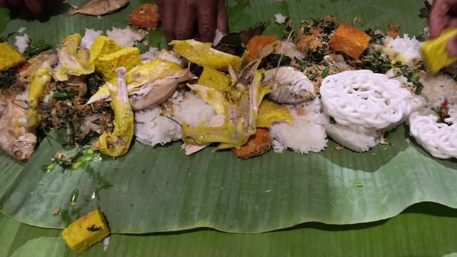 Traditional Indonesian communal meal served on banana leaf featuring rice, chicken, fish, tofu, vegetables, flavorful spices.