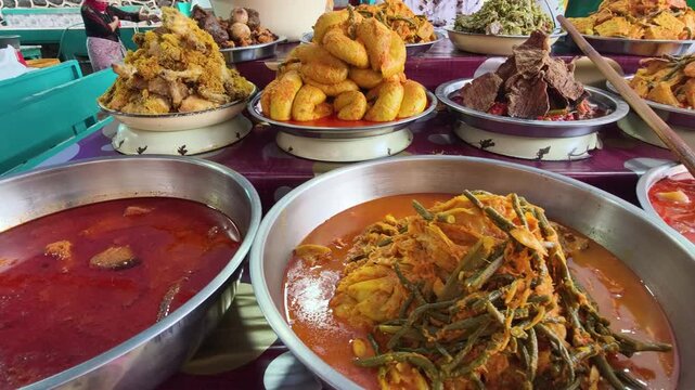 A colorful display of Nasi Kapau dishes at a local food stall. The assortment includes Gulai Tambusu, rendang, vegetables cooked in coconut milk curry, and other Minangkabau specialties.