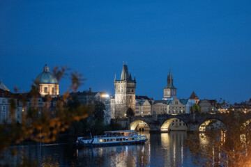 Fototapeta premium Illuminated charles bridge, old town bridge tower, and boat cruising vltava river in prague at twilight