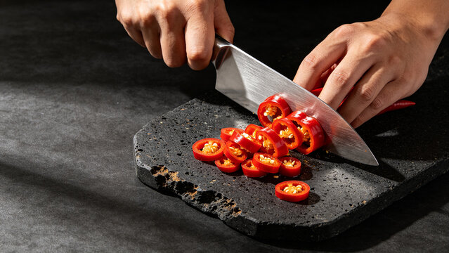 Hands slicing hot red chili pepper with Damascus chef knife