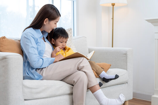 Asian Mother and Little Son Sitting on Sofa Reading Book