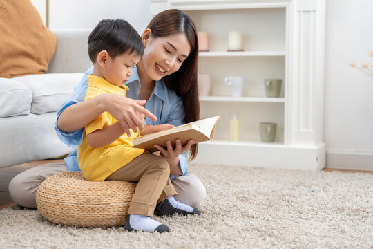 Asian Mother Reading Book to Her Little Son in Living Room