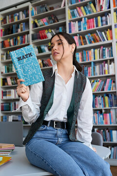 Smart young woman studying math in a college library filled with books