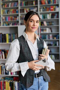 Smart young woman studying in a cozy college library with a stack of books