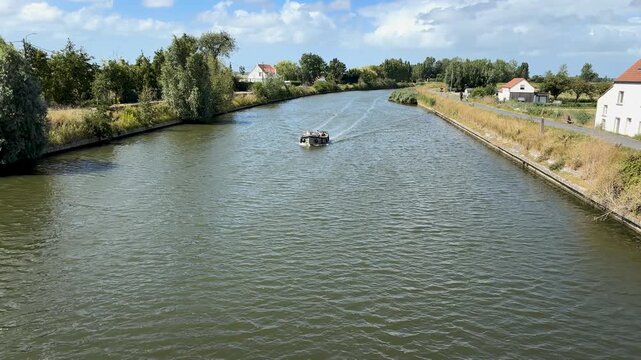Happy people waving from pleasure boat on the Yser River, fun recreational activity in West Flanders, Belgium on a sunny summer day.