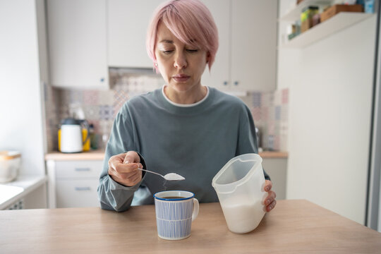 Mature woman adding spoonful of sugar to cup of aromatic morning coffee, uncontrolled intake of sweeteners, female putting additional spoon of sugar in beverage, dangerous fast dopamine addiction.