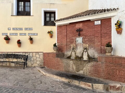 Fuente tradicional en una calle de un pueblo andaluz con macetas y mensaje sobre la primavera
