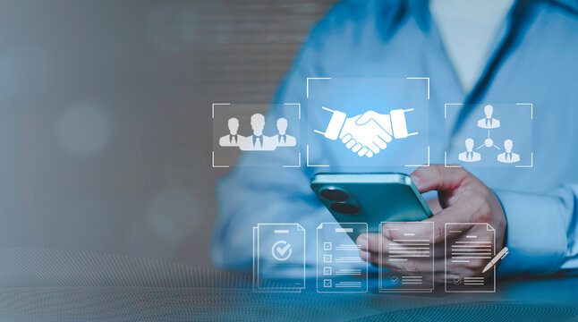 Concept of partnership agreement, professional CRM and human resources coordination. Hand using smartphone with icons for business handshake deal, procurement, team management and verified documents