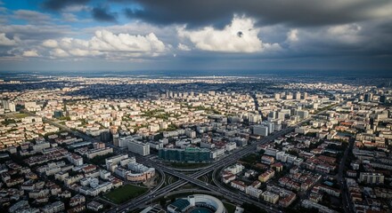 Fototapeta premium Expansive aerial view of a sprawling modern city skyline with complex road infrastructure under a dramatic cloudy sky
