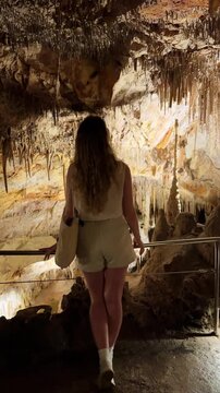 female tourist visiting cave, enjoying admiring nature dark caves stalactites and stalagmites rock formations. fantastic vertical video Cuevas del Drach. silhouette woman back view, walking looking.