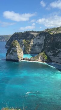 A scenic view of rocky cliffs by the turquoise sea under a clear blue sky. The landscape showcases natural beauty and coastal features.