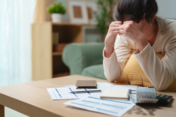 Stressed woman reviewing bills and financial documents at home, feeling worried about debt and...