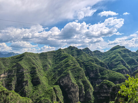 A scenic view of the Yesanpo mountains covered in dense greenery under a blue sky with dramatic clouds.