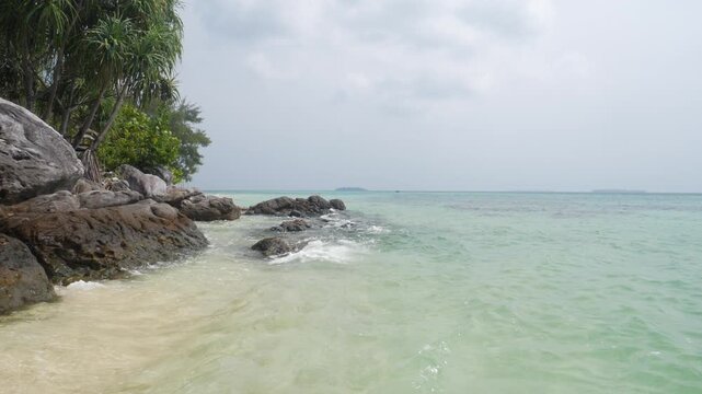 Slow motion: waves on rocky tropical shoreline with crystal clear turquoise sea in Karimunjawa National Park Indonesia lush vegetation and tranquil island scenery