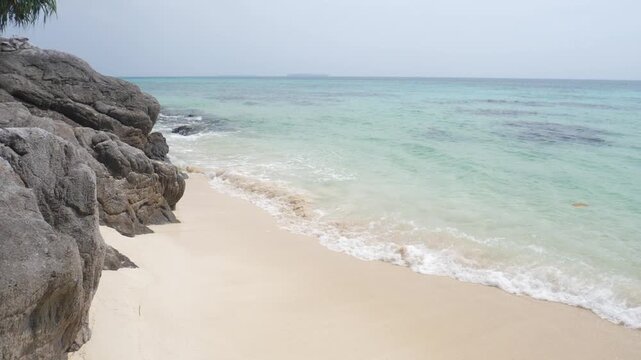Slow motion: waves on rocky tropical shoreline with crystal clear turquoise sea in Karimunjawa National Park Indonesia lush vegetation and tranquil island scenery