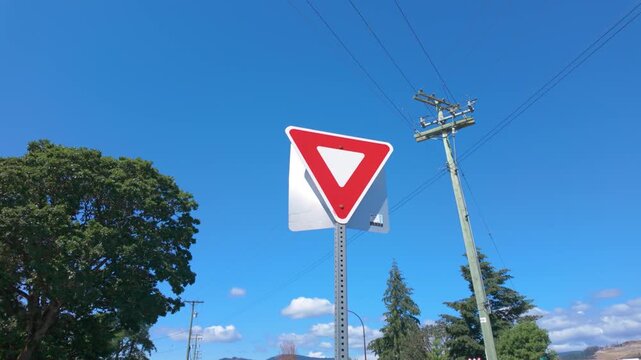 Low angle tracking shot of a standard red and white triangular yield sign.