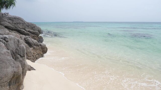 Slow motion: waves on rocky tropical shoreline with crystal clear turquoise sea in Karimunjawa National Park Indonesia lush vegetation and tranquil island scenery