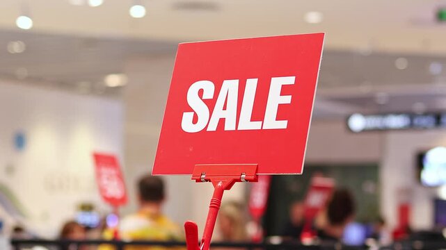 Red sale sign in modern shopping mall with blurred shoppers in background, seasonal retail discount promotion, consumer spending, marketing campaign and commercial shopping concept