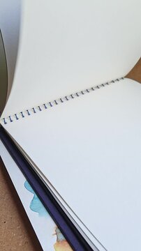 Hand flipping through blank sketchbook with clean white pages, open drawing pad inviting creativity, inspiration for artists, designers and creative work, close-up vertical video