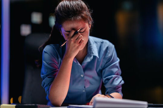 Stressed young adult woman working late night in office facing p