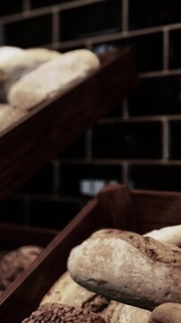 Breads are placed on wooden shelves in a bakery shop. The breads are of different types and shapes, fresh from the oven, ready for customers to buy. The setting is cozy.