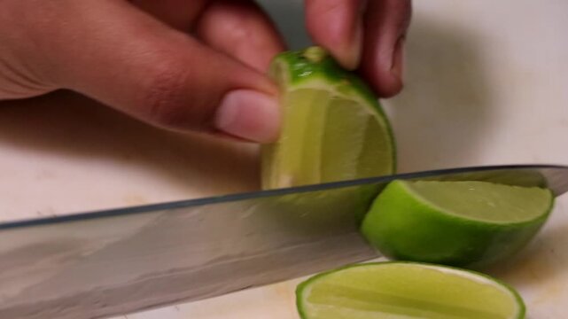 Mano cortando lim&oacute;n agrio sobre tabla de cocina blanca. Primer plano de lim&oacute;n verde siendo cortado con cuchillo. Cortes de lim&oacute;n agrio para preparaci&oacute;n de alimentos. Cocinero cortando lim&oacute;n.