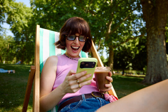 Excited woman stares at her phone while relaxing outdoors