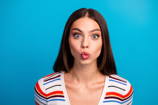Portrait of a young chic woman with a playful pout against a bright blue background wearing a striped casual sweater for fashion lifestyle and advertising use